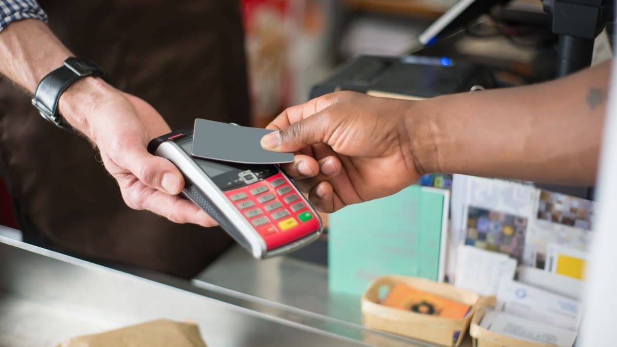 A contactless bank card tapped on a payment terminal at a Malaysian shop counter