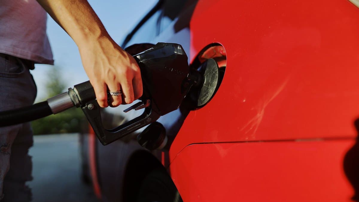 A person refuelling a car, holding the fuel pump nozzle at a petrol station