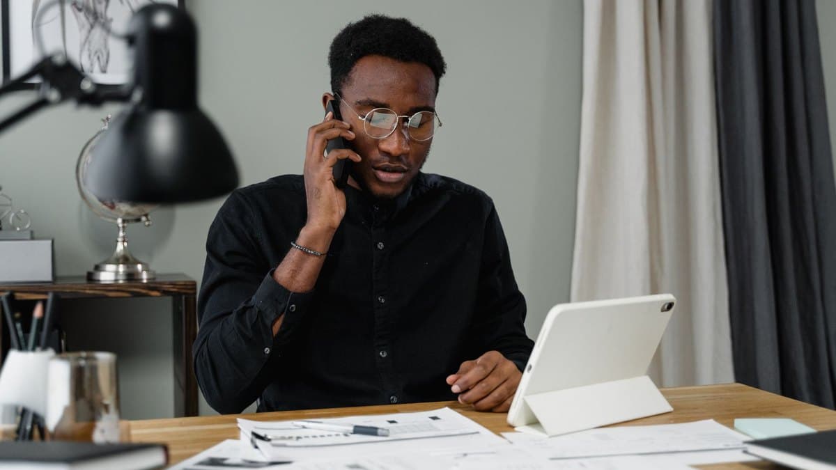 A cardholder on the phone at a home desk with statements and a tablet in front of him