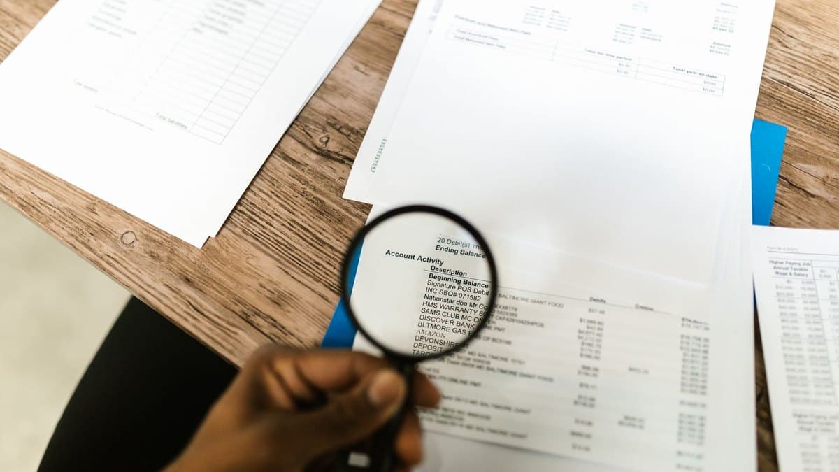 A hand holding a magnifying glass over the account-activity lines of a financial statement